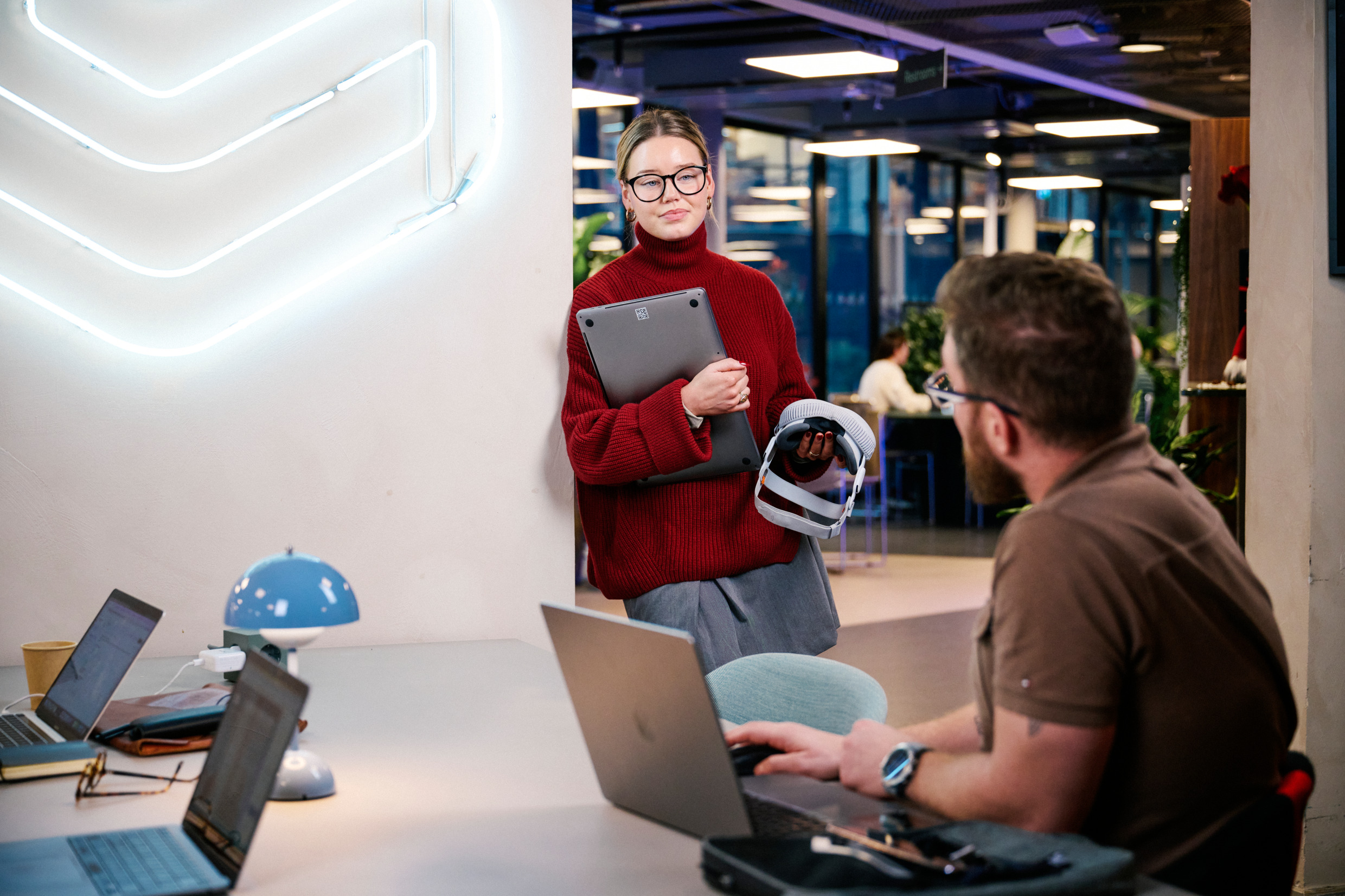 An office environment with a man and a woman talking surrounded by tech gear.
